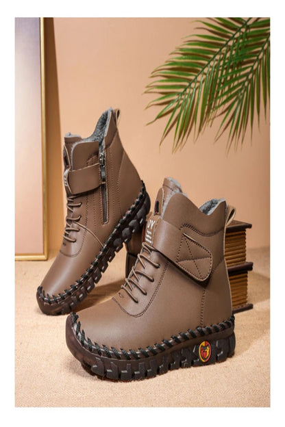 Brown leather boots with a textured sole on a beige surface with a plant in the background