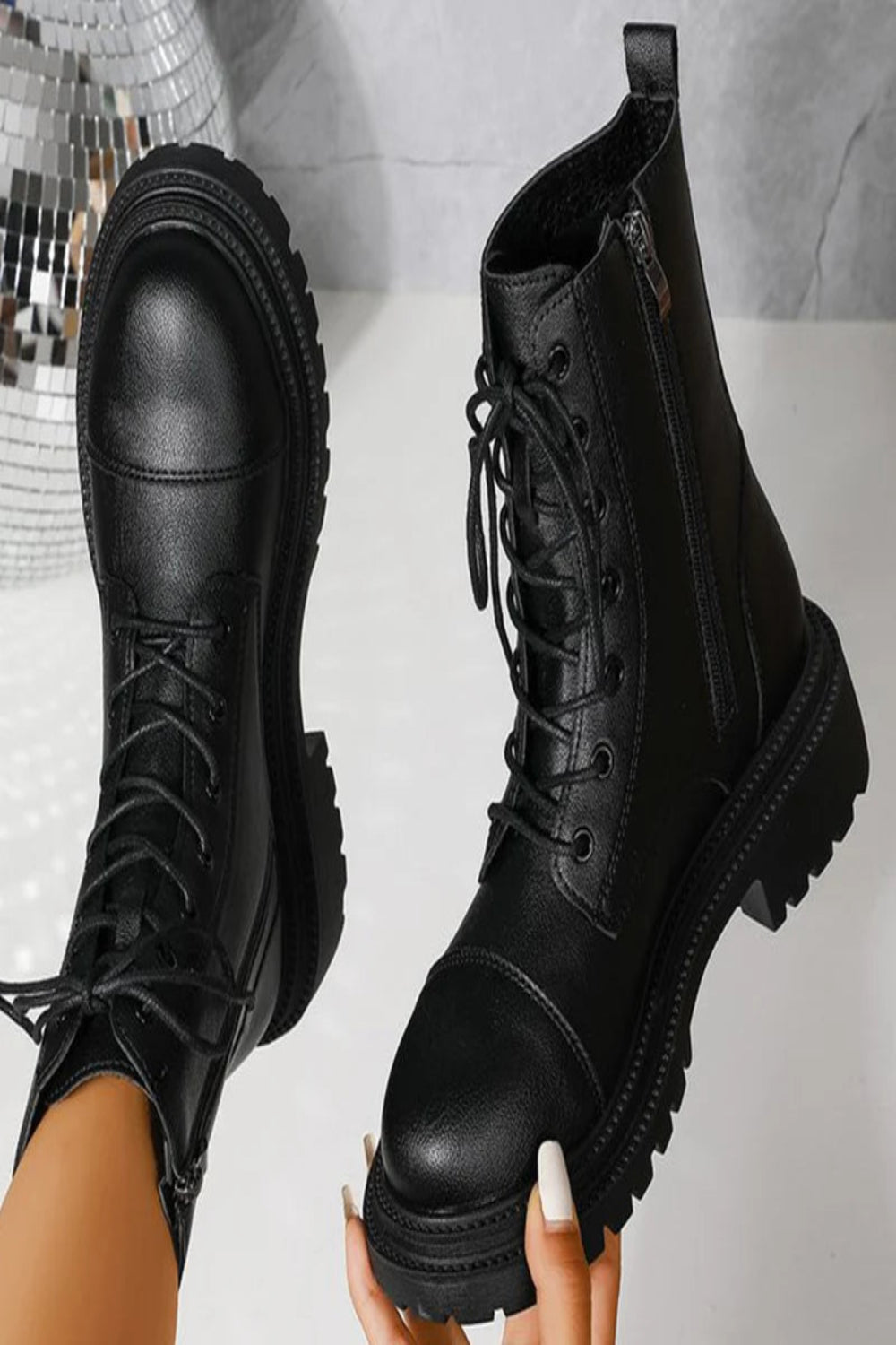 Black leather boots with a platform sole held by a hand against a neutral background