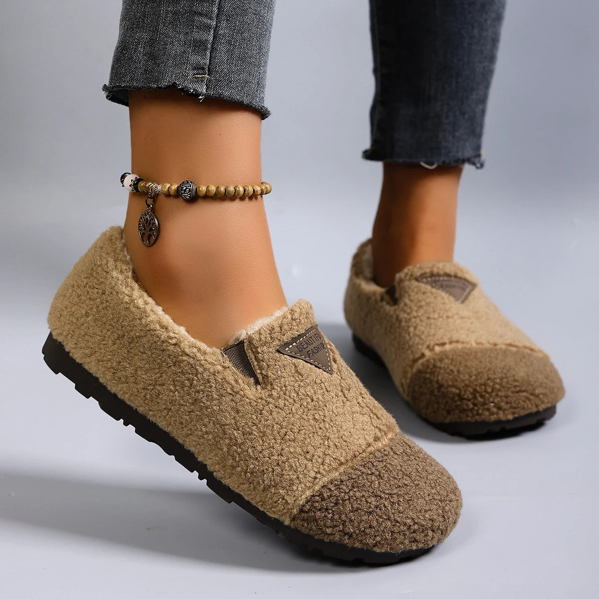 Beige slippers worn with rolled-up jeans on a neutral background