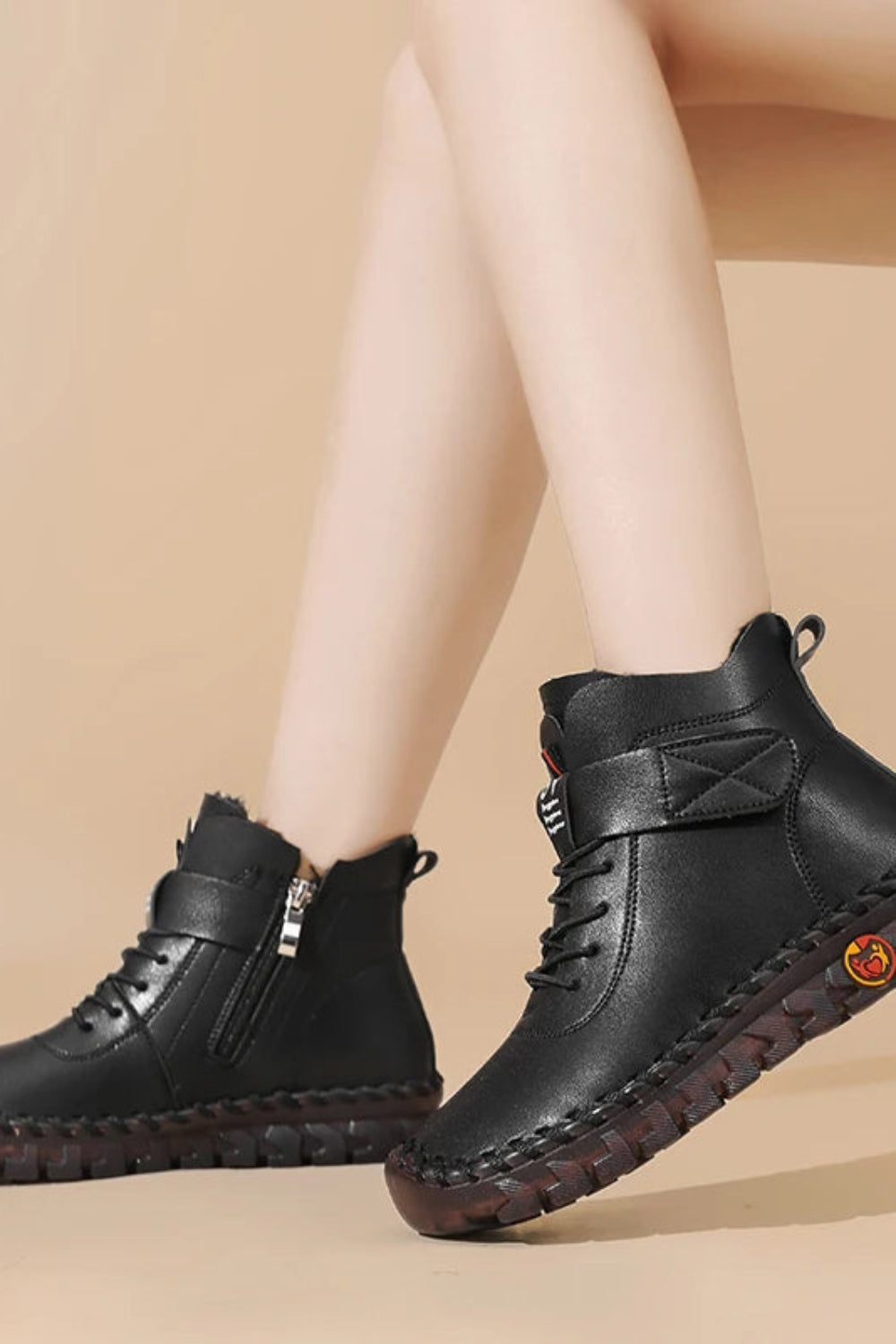 Black leather boots worn by a person on a beige background