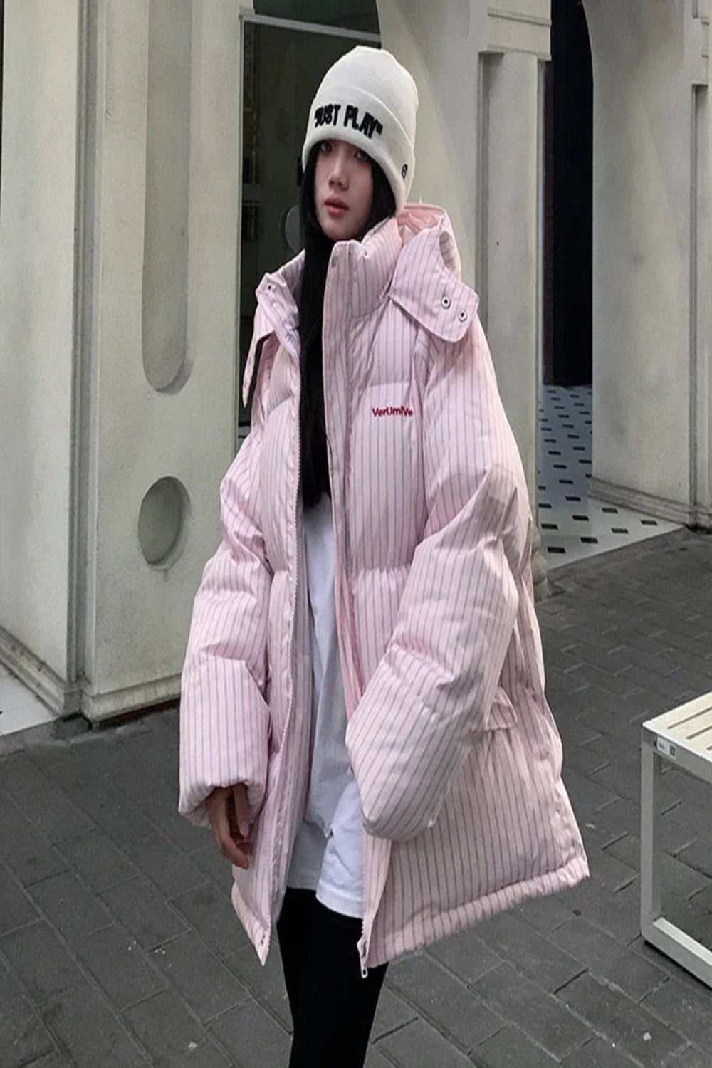 Person wearing a pink puffer jacket and white beanie outdoors.