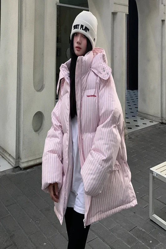 Person wearing a pink puffer jacket and white beanie outdoors.