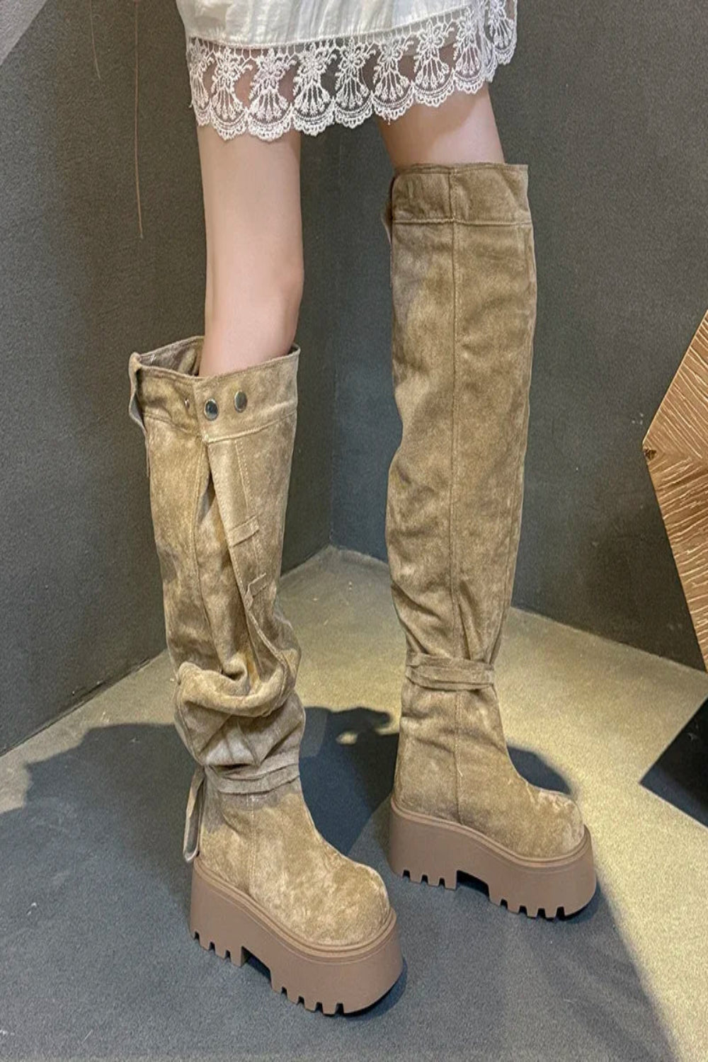 Tan knee-high boots worn with a white lace skirt on a neutral background