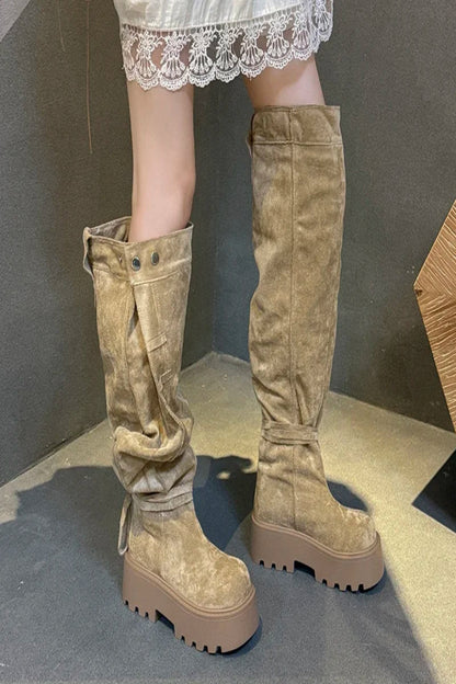 Tan knee-high boots worn with a white lace skirt on a neutral background