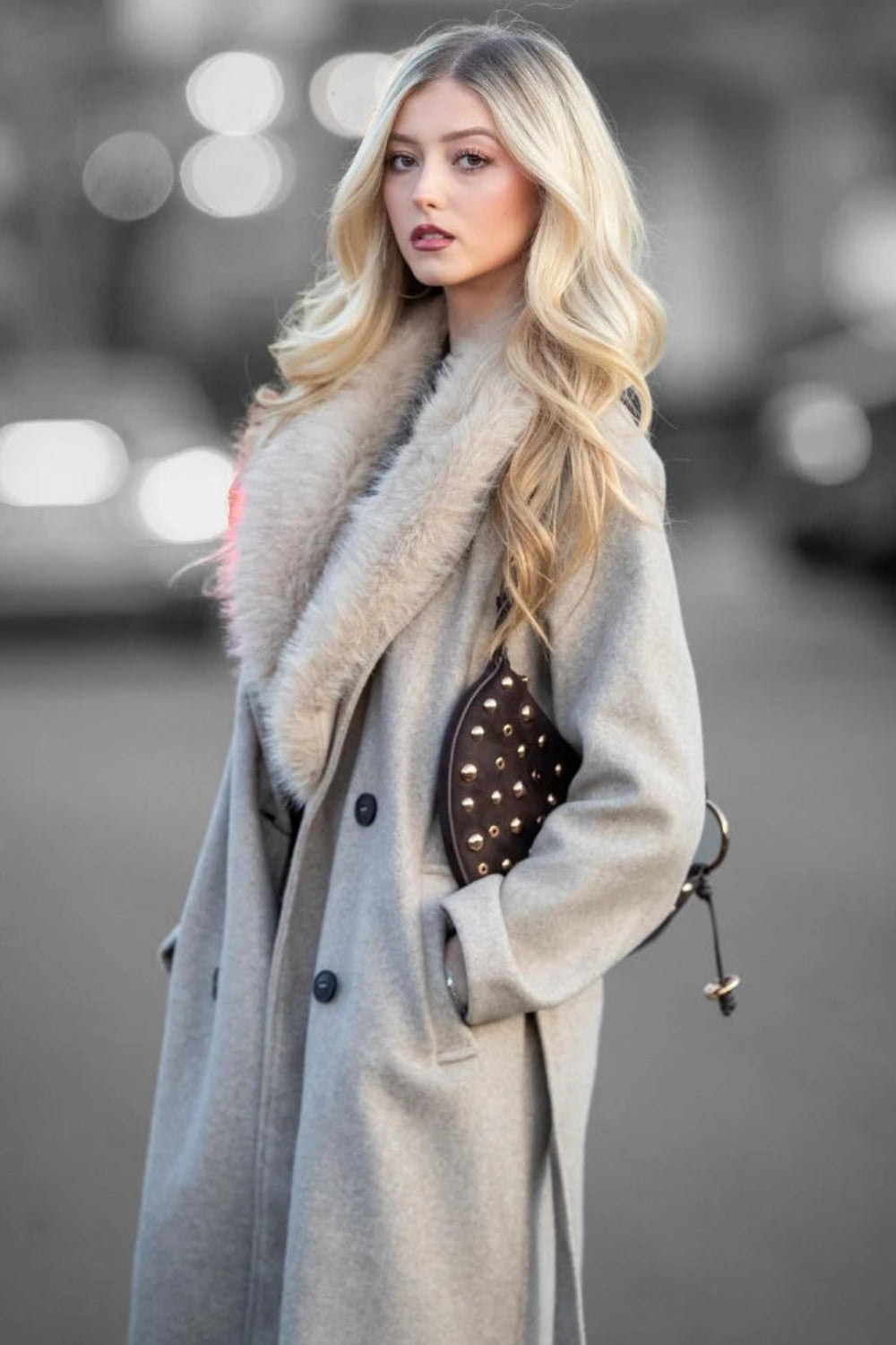 Woman wearing a long coat with a fur collar on a blurred street background