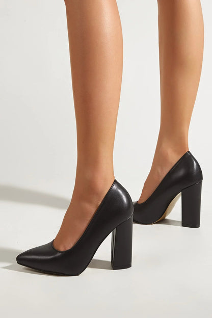 Black high-heeled shoes worn by a person on a light background