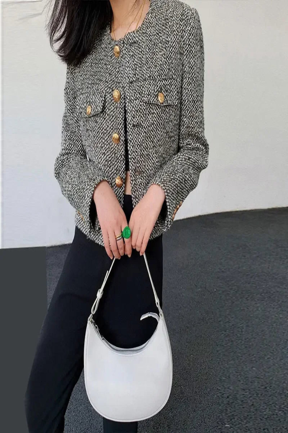 Person wearing a textured jacket with gold buttons holding a white handbag.