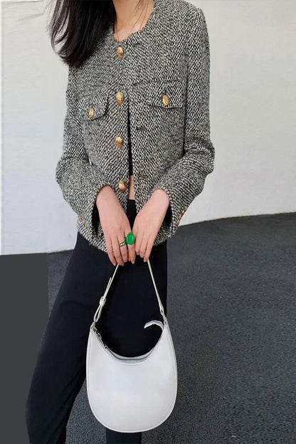 Person wearing a textured jacket with gold buttons holding a white handbag.