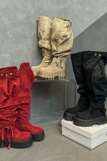 Three pairs of boots in red, beige, and black on a gray concrete floor.