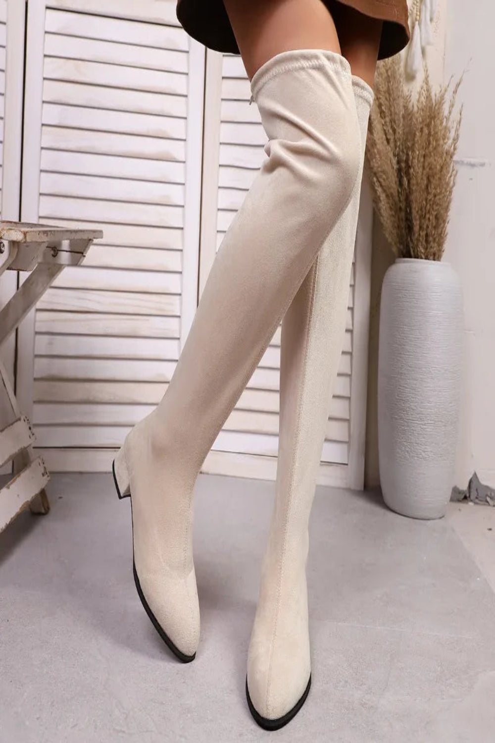 White knee-high boots worn by a person indoors with a neutral background