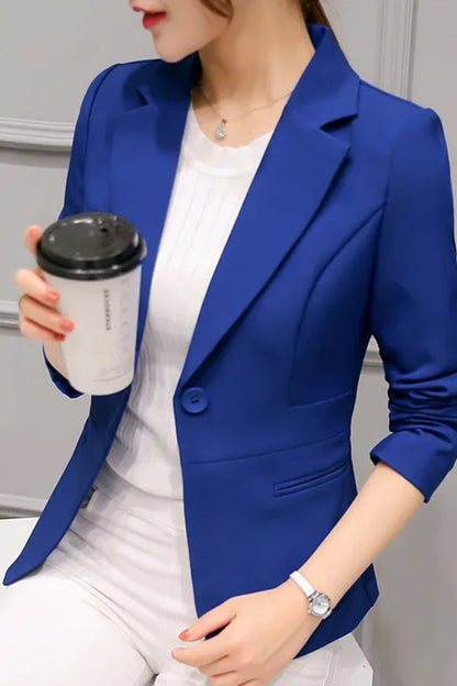 Person wearing a blue blazer holding a coffee cup against a gray wall.