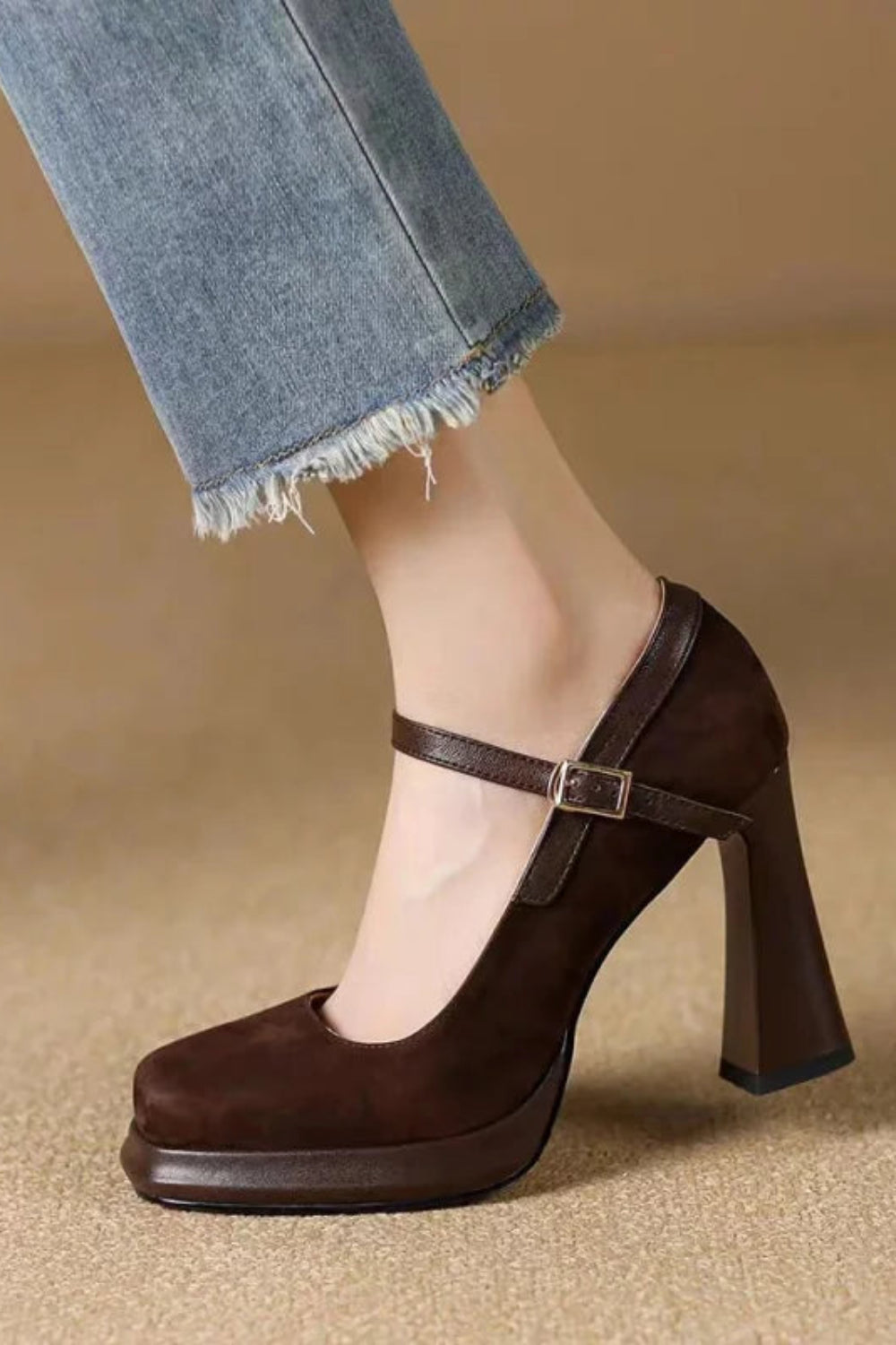 Brown high-heeled shoe worn with light blue jeans on a beige background