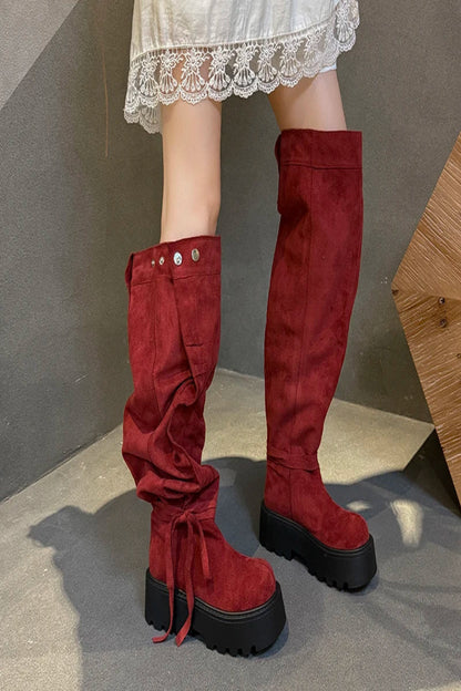 Red platform knee-high boots worn with a white lace dress on a neutral background