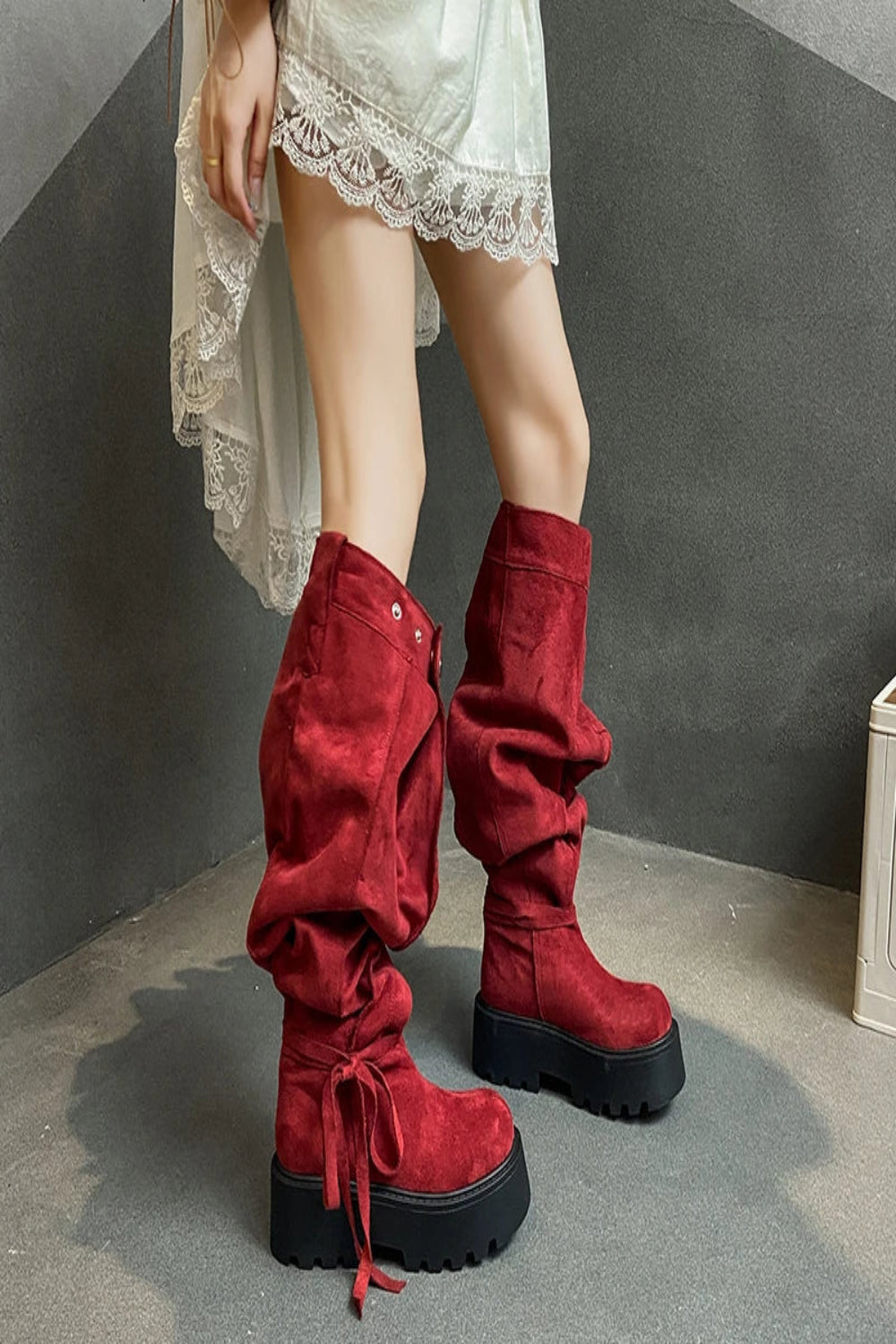 Red platform boots worn with a white lace dress on a gray background
