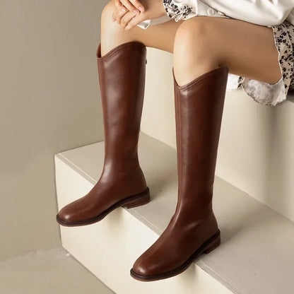 Brown knee-high boots worn by a person sitting on a white step.