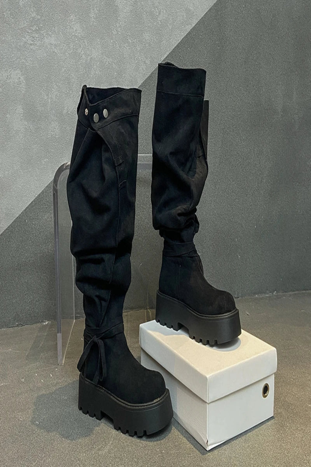 Black knee-high boots on a white box with a gray background