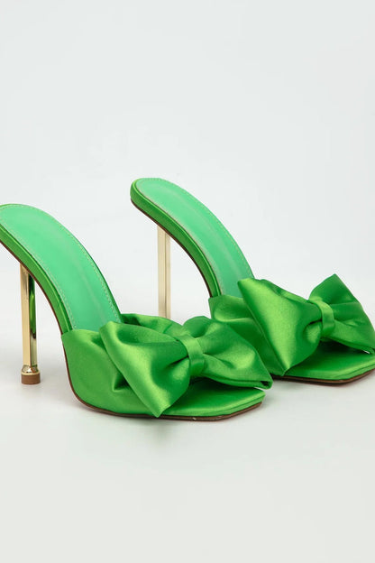 Green high-heeled shoes with large bows on a white background