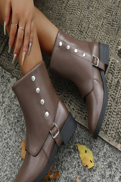 Brown leather boots with silver buckles on a textured surface