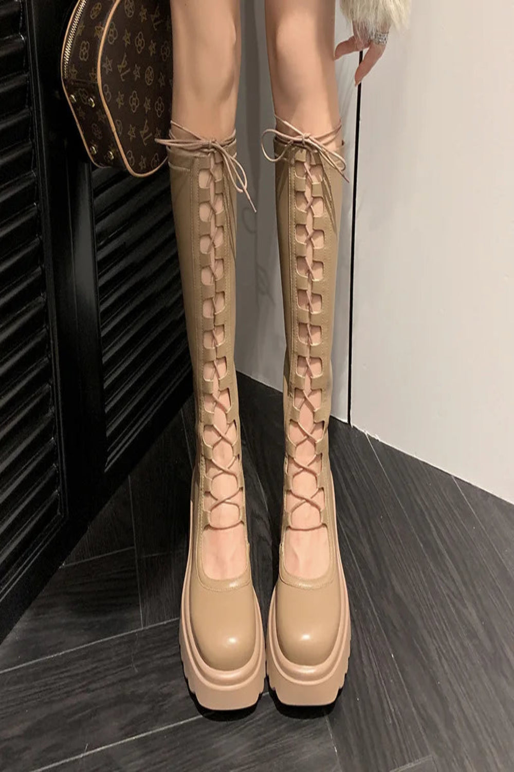 Beige knee-high boots with platform sole on a dark floor.