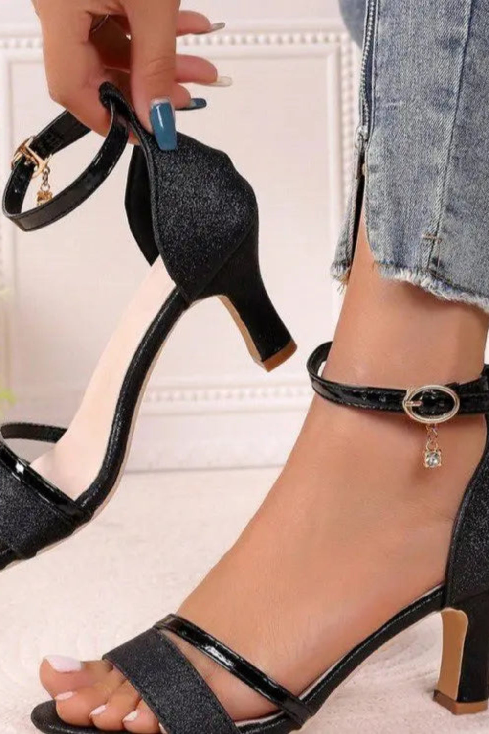 Black glittery high-heeled sandals with decorative straps worn by a person.