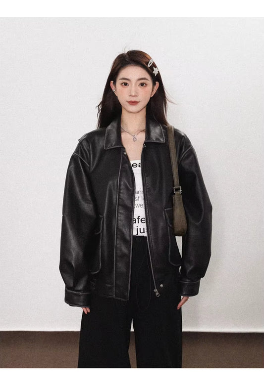 Person wearing a black leather jacket and white shirt with text, standing against a plain background.