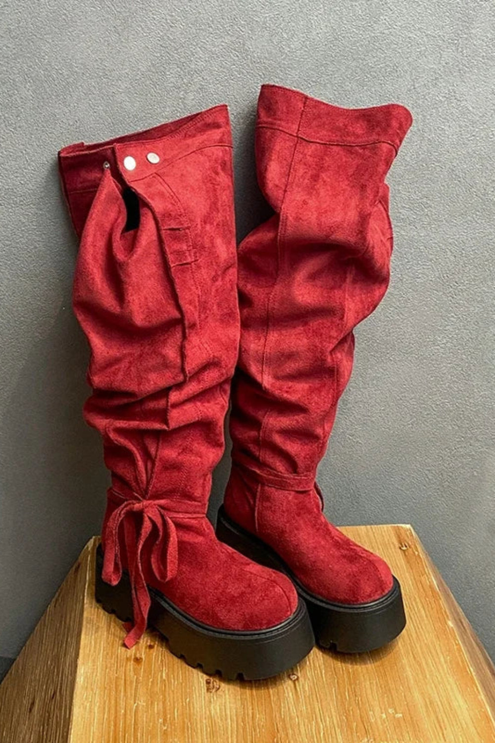 Red suede knee-high boots on a wooden block against a gray background