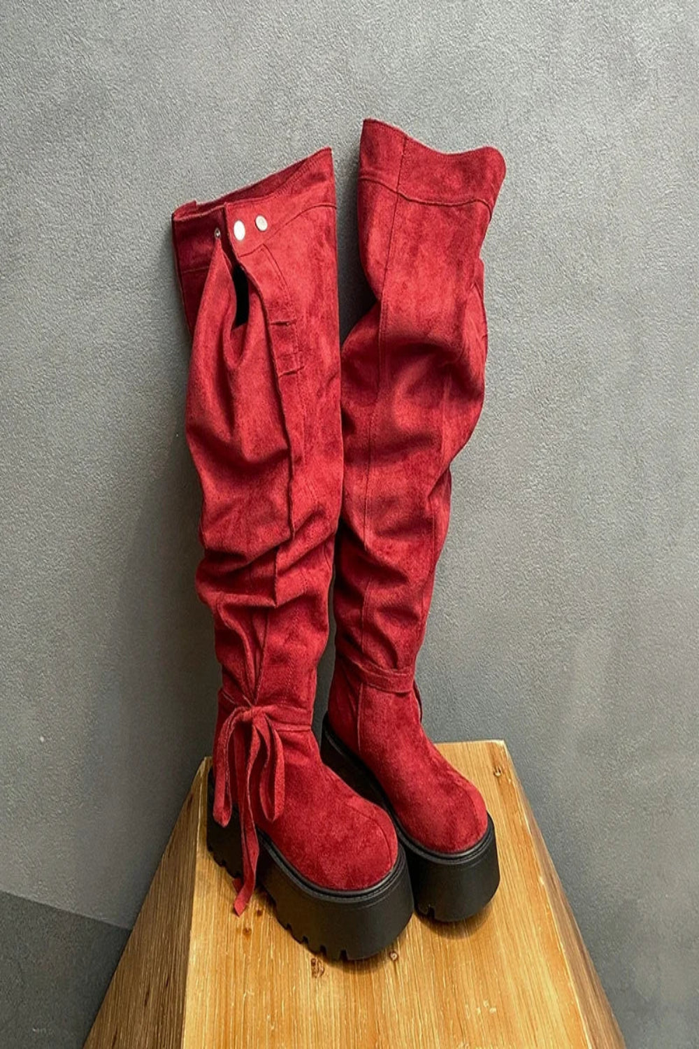 Red suede knee-high boots on a wooden block against a gray background
