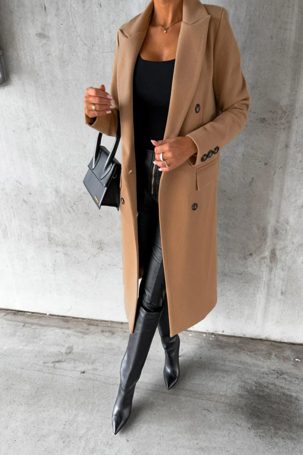 Person wearing a beige coat and black boots against a concrete wall.