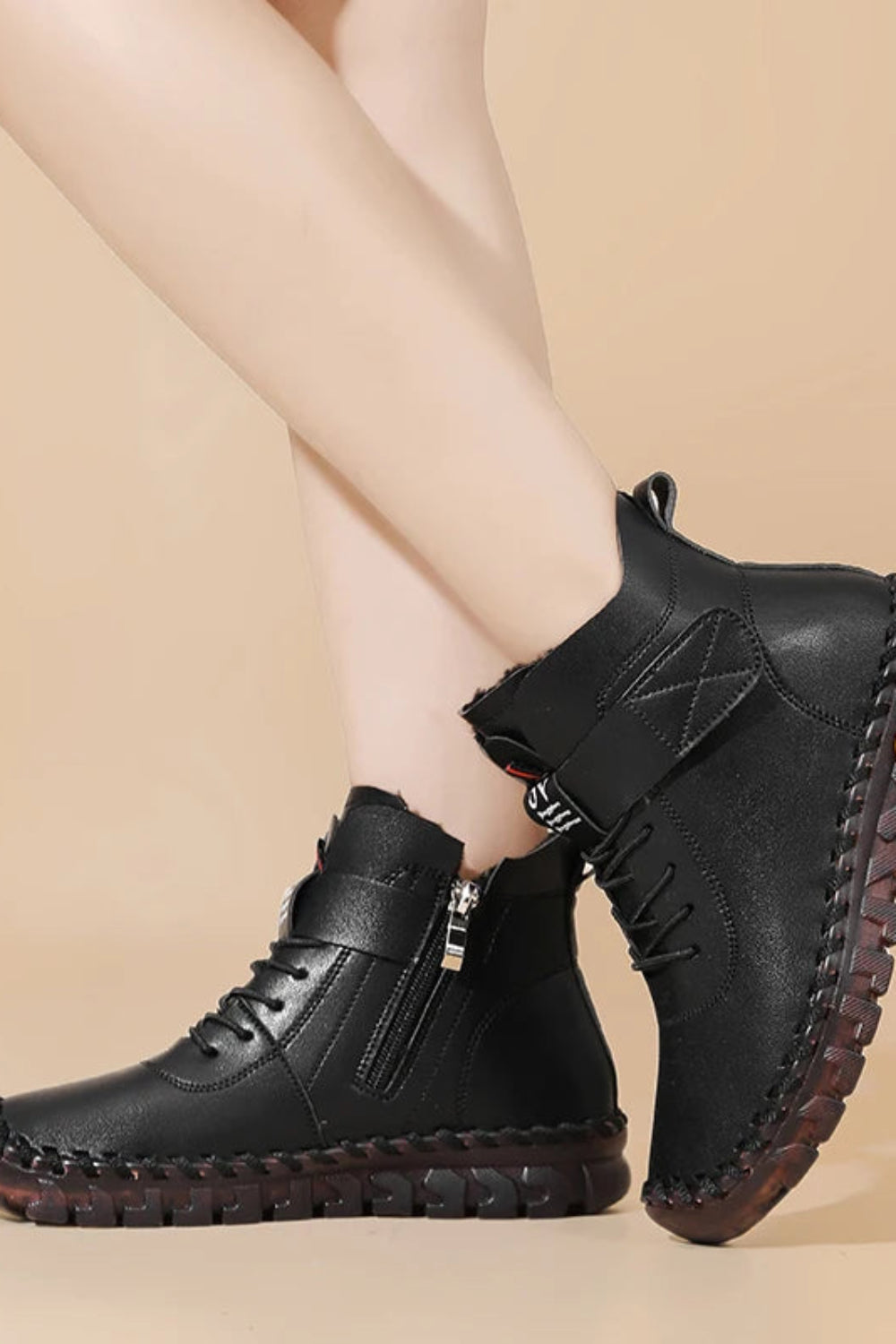 Black leather boots worn by a person on a beige background