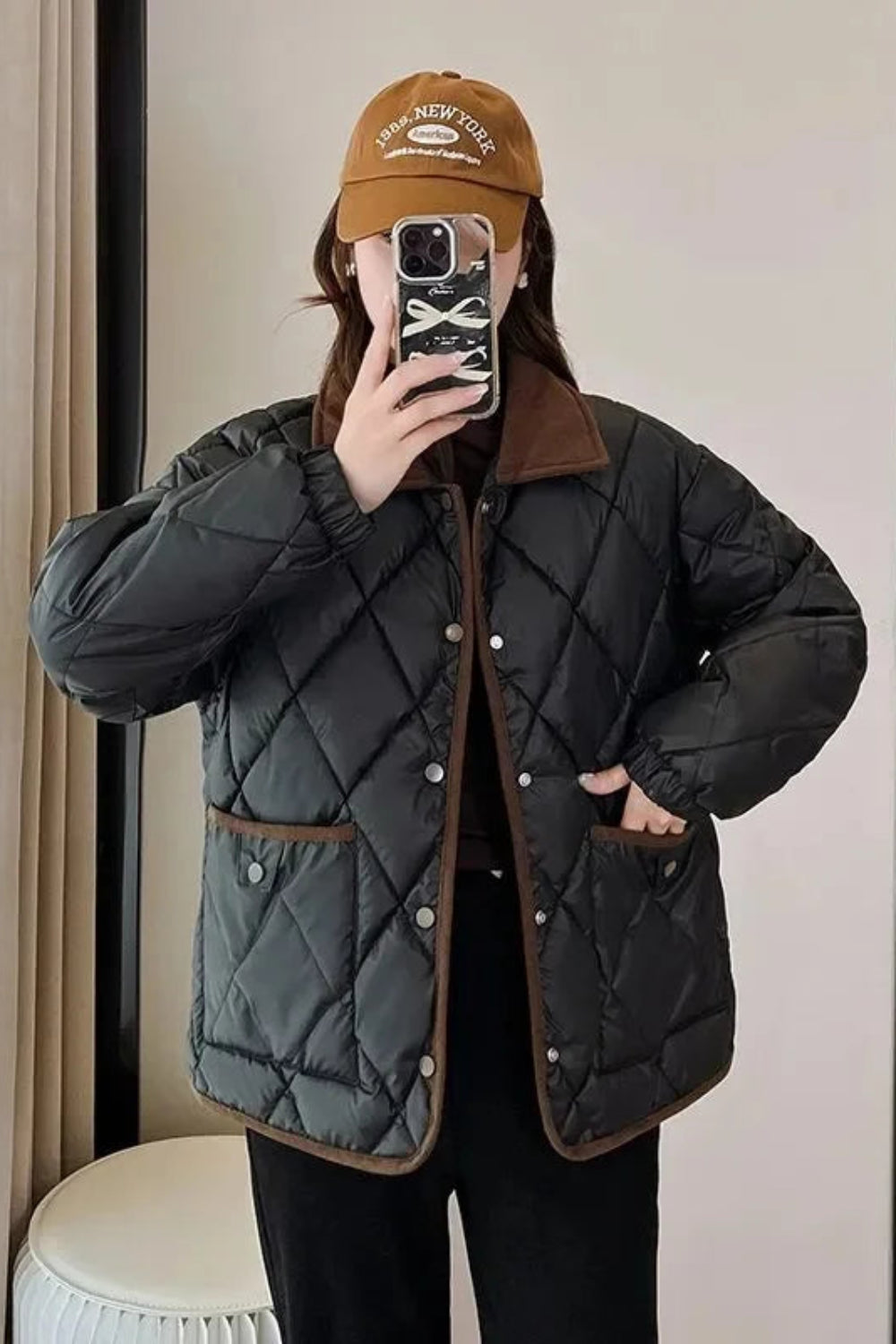 Person wearing a black quilted jacket with brown accents taking a mirror selfie.