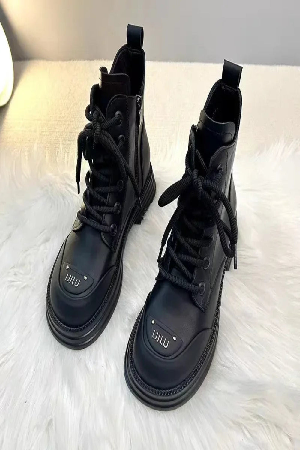 Pair of black lace-up boots on a white fur surface