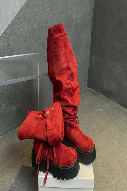 Red suede boots with black soles on a white platform against a gray background