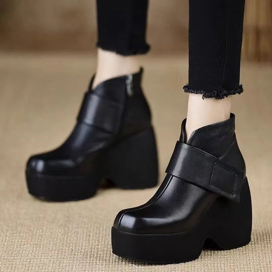 Black platform ankle boots worn with black pants on a beige surface