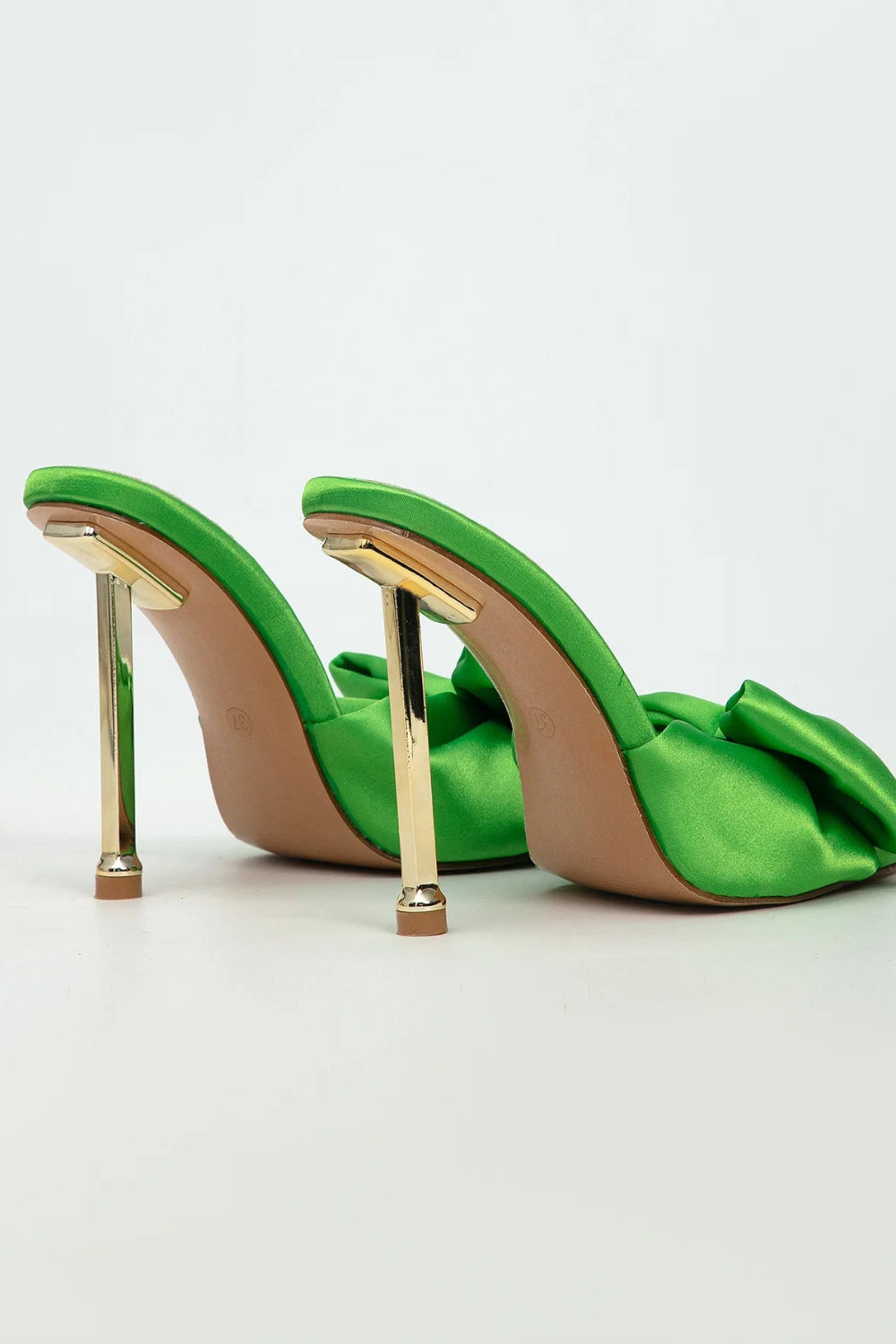 Green high-heeled shoes with gold accents on a light gray background