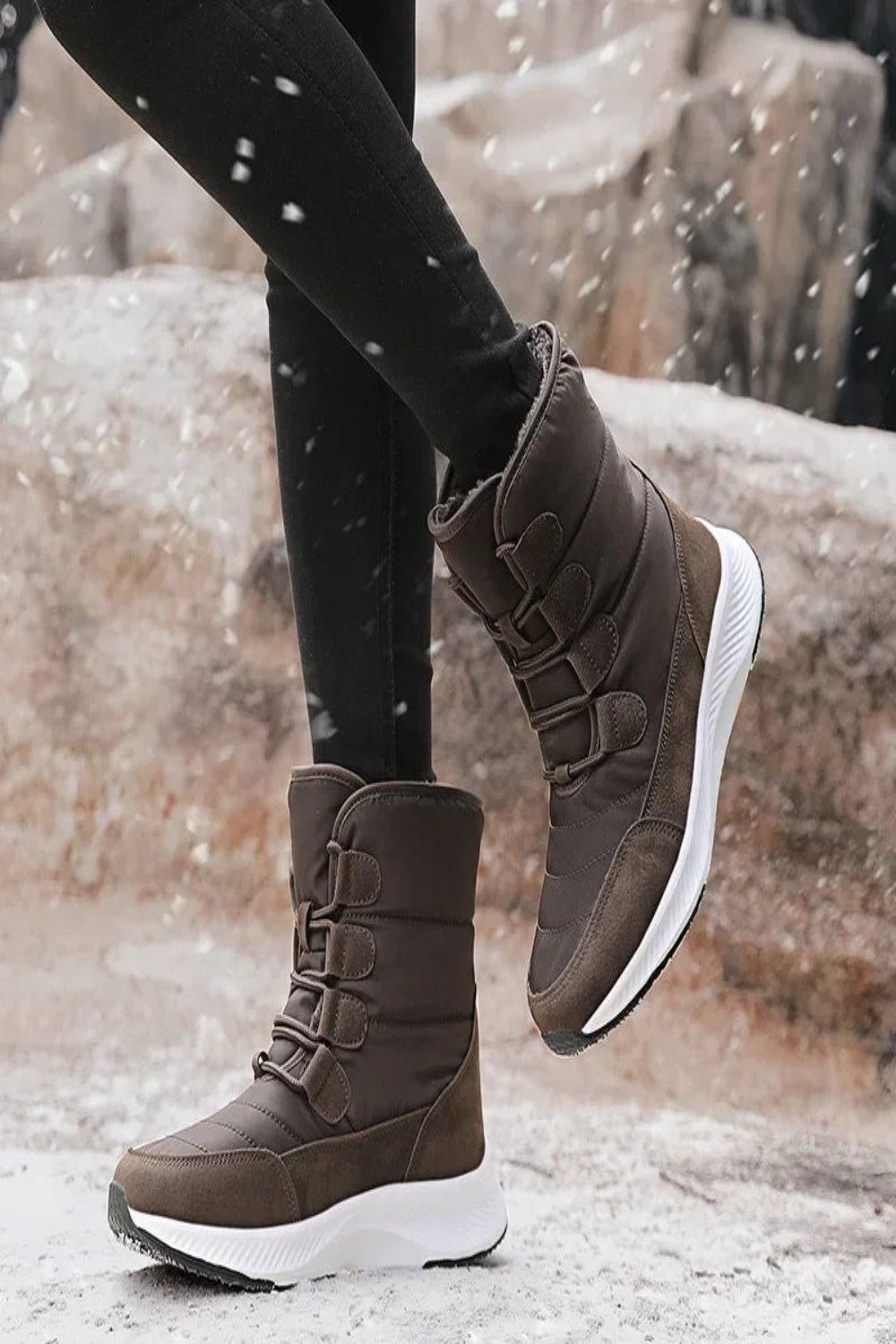 Brown winter boots with white soles worn by a person on a snowy ground.