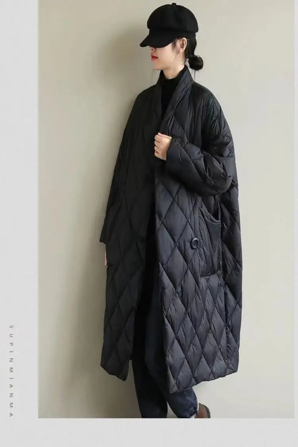 Person wearing a long black quilted coat against a plain background