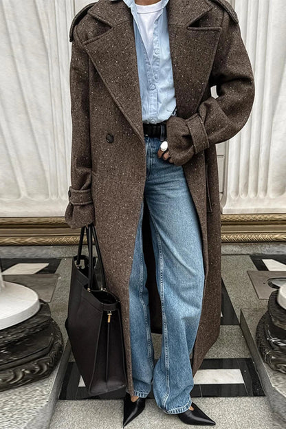 Person wearing a brown coat, light blue shirt, and jeans in an indoor setting.