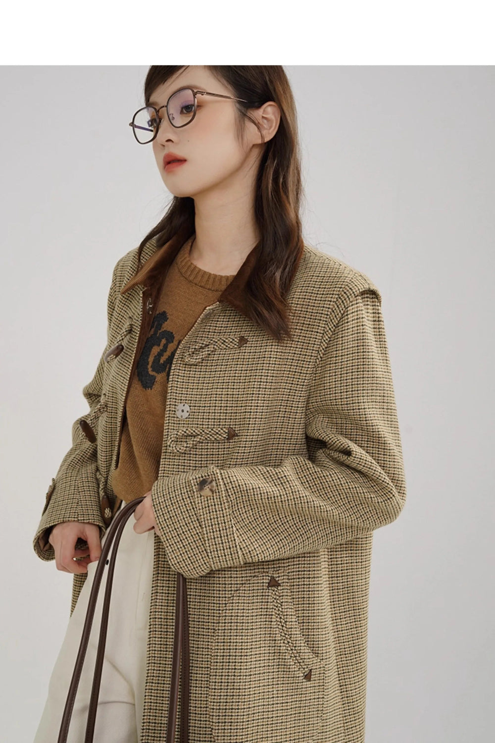 Woman wearing a plaid coat over a brown sweater with a white background