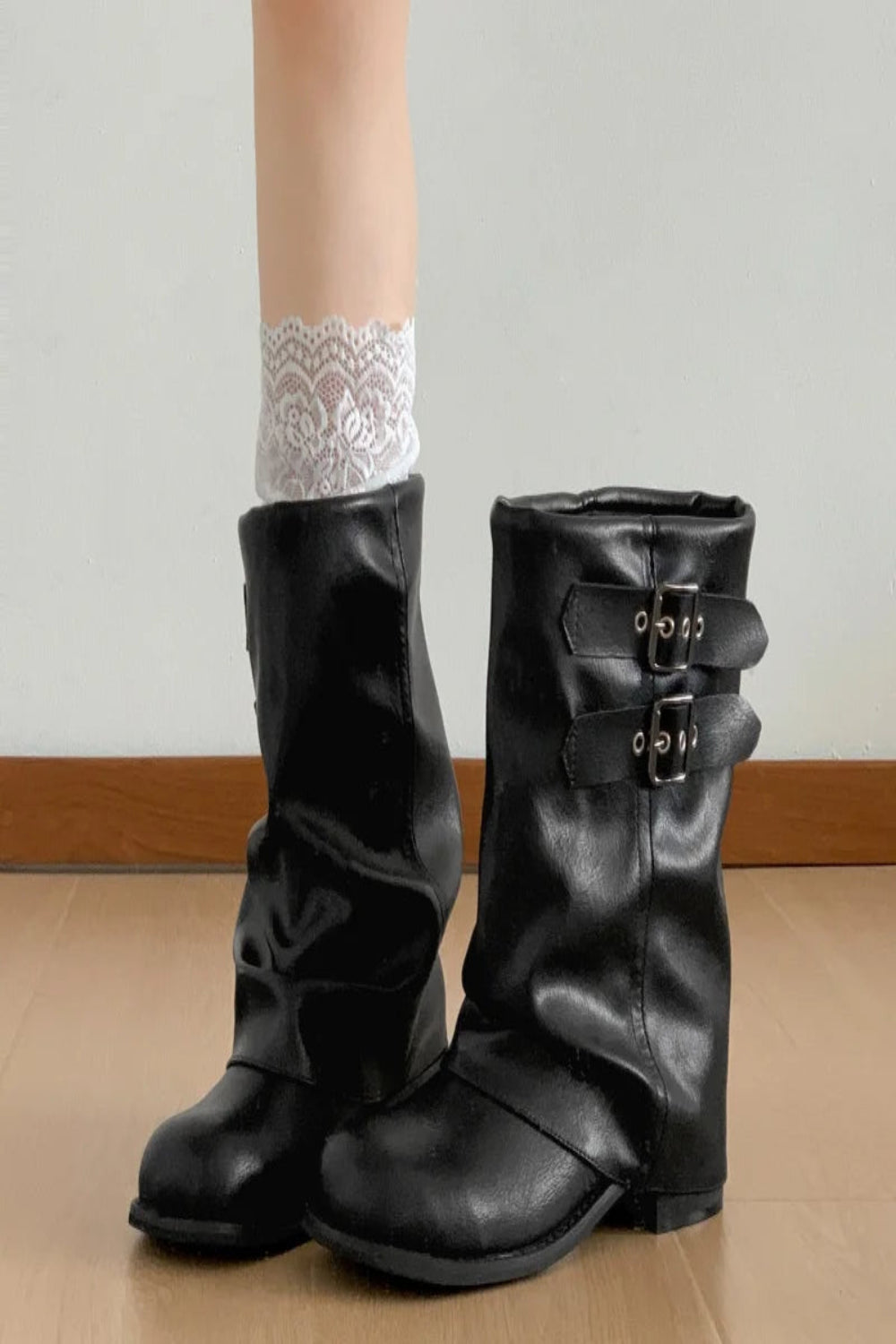 Black leather boots with buckles worn by a person on a wooden floor.