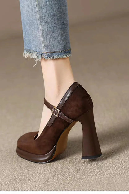 Brown high-heeled shoe worn with a denim leg, on a neutral background