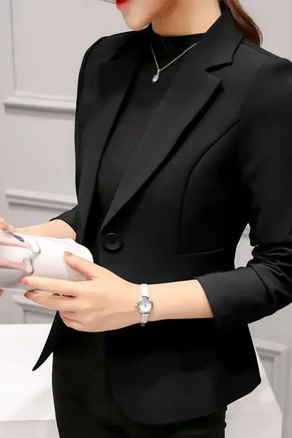 Person wearing a black blazer holding a white object against a neutral background