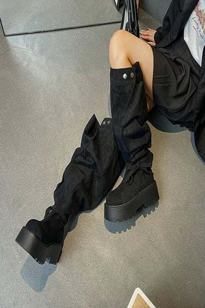 Person wearing black knee-high boots sitting on a concrete floor.