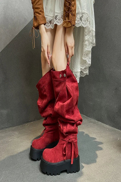 Red platform boots worn with a white lace dress against a gray background