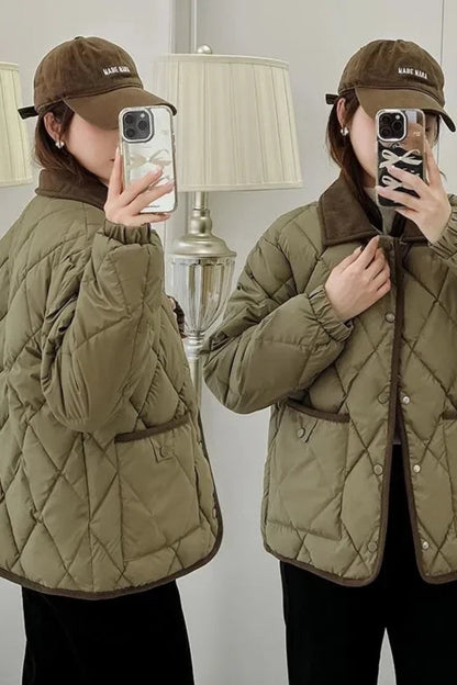 Person wearing a quilted green jacket and brown cap taking a mirror selfie.
