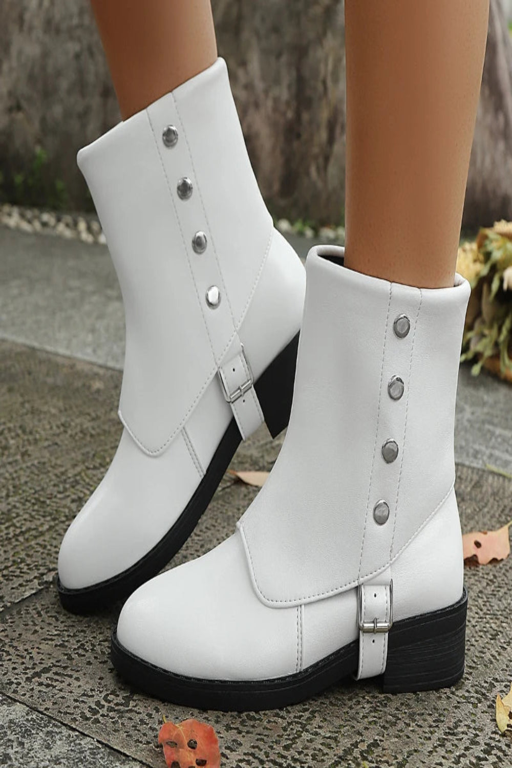 White ankle boots with black soles worn by a person on a textured surface.
