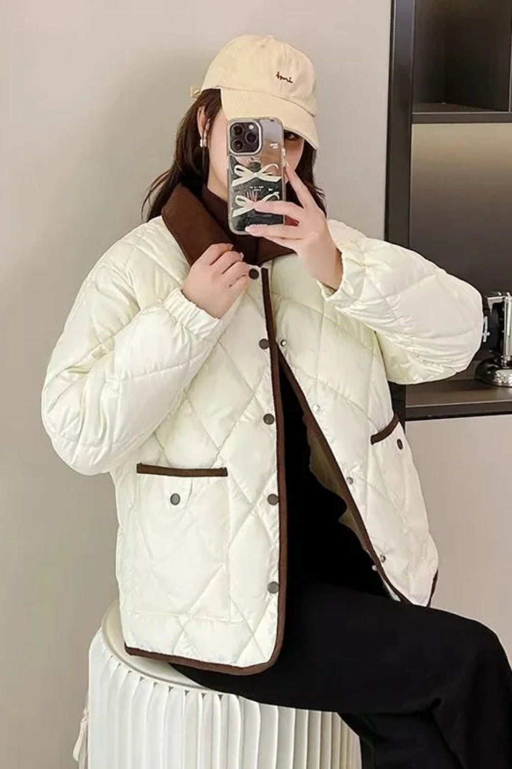 Person wearing a white quilted jacket with brown accents, taking a mirror selfie.