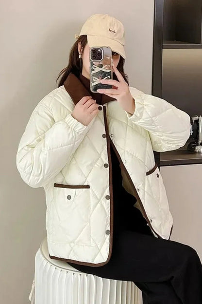 Person wearing a white quilted jacket with brown accents, taking a mirror selfie.