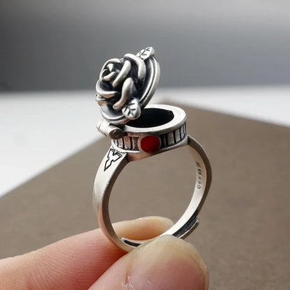 Silver ring with a rose design held by a hand against a neutral background