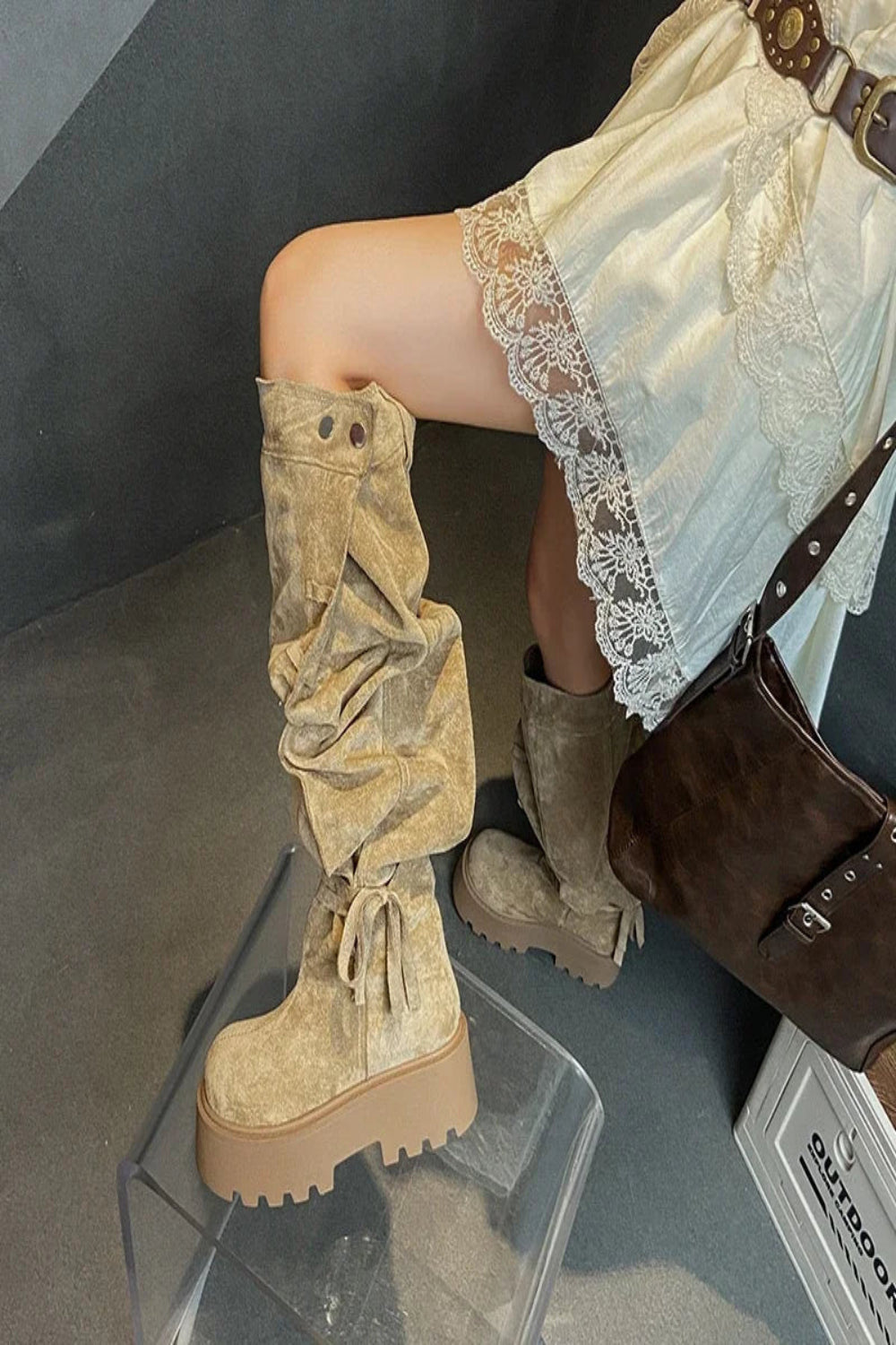 Person wearing beige suede knee-high boots with a lace dress and brown handbag.