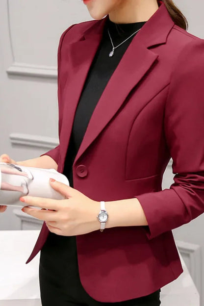 Person wearing a burgundy blazer over a black top, holding a white object.